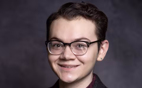 A young man with short brown hair and glasses smiles for a portrait.