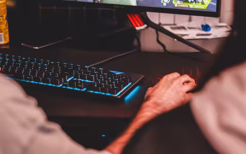 A hand hovers over a computer mouse next to a lit-up keyboard and computer screen.