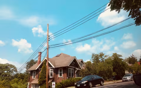 A black car in front of a brown house next to green trees.