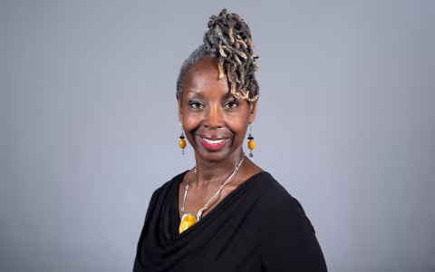 Professor Kyra Gaunt wearing a black blouse and yellow and silver earrings and a necklace, with her hair piled on top of her head.