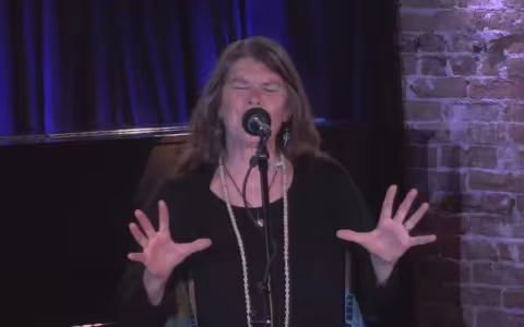 storyteller at mic performs with eyes closed and hands extended