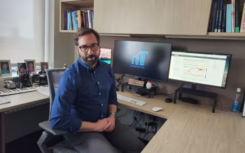 Brian Rose sits at his desk in front of dual computers on the Project Pythia website.