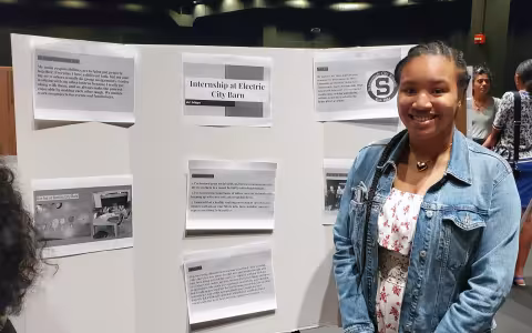 Schenectady's Ari Mayo stands in front of a poster she created describing her internship with Electrict City Barn.