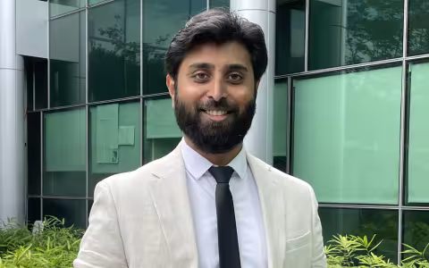 Arun Chandrasekaran wears a cream colored linen suit jacket and dark blue tie for a portrait outside the RNA Institute.