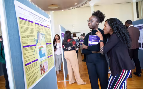Two people look at a research poster in an auditorium of research posters.