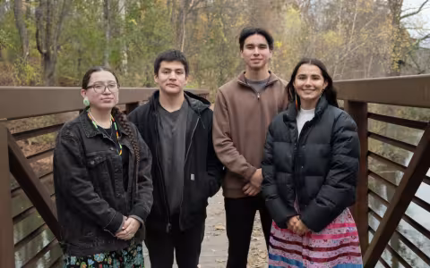 Two young men and two young women stand on a bridge over Parker Pond on the UAlbany campus on an overcast fall day.