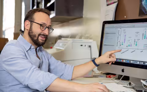 Paolo Forni smiles and points at a computer monitor displaying undreadable text.