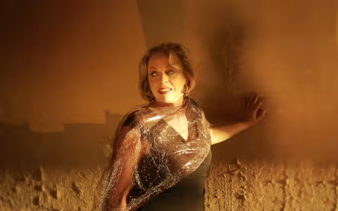 womans places her hand on a gold colored wall while looking over her left shoulder