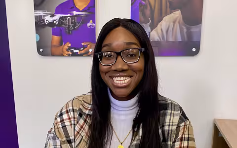Maimouna Camara, a UAlbany MSW student, sits at a desk and smiles.