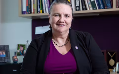 University at Albany’s College of Nanotechnology, Science, and Engineering (CNSE) Dean Michele J. Grimm sits at her desk with a row of books behind her.