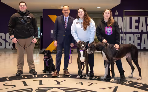 Two men, two women and three dogs line up in the University Hall atrium for a photo.