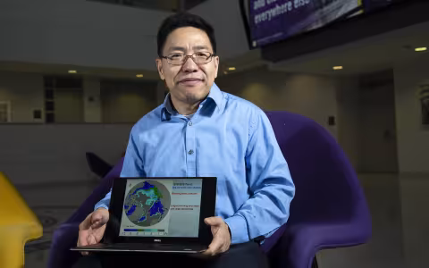 Aiguo Dai holds a laptop with a globe graphic displayed inside University Hall.