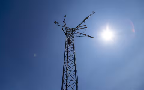 The sun shines behind the top of a New York Mesonet station weather tower.