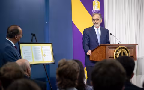 A man in glasses addresses a group from a podium