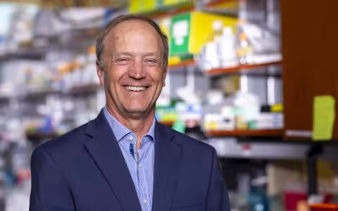 A smiling man in a blue blazer stands in a laboratory.