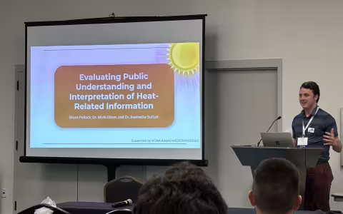 Bruce Pollock uses a projector screen and podium to present on heat warning communication. 