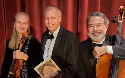 Three musicians sit smiling at the camera