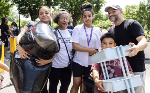 A family of five poses for a photo on Move-In Day at UAlbany. A young woman is carrying a large garbage bag of belongings while a young boy lifts a shelf.