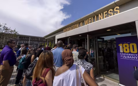 A group of people head into a building entrance with the words "Recreation & Wellness" in metal letters above the door. 