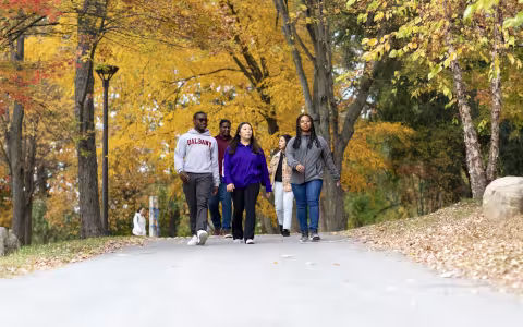 a group of 5 students walk on a path under trees with yellow leaves