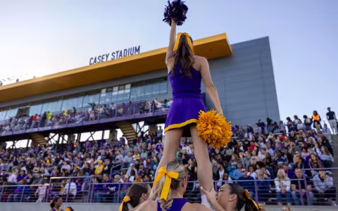 A UAlbany cheerleader waves her pom-poms while hoisted in the air at a football game in Casey Stadium.