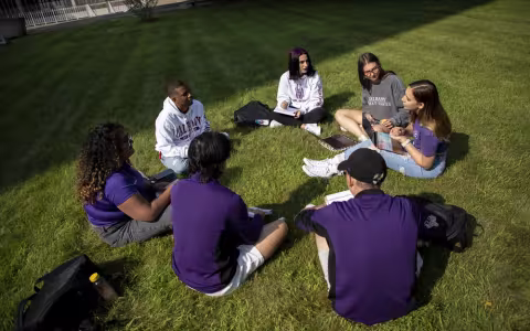 Students seated in a circle on the grass outside building 