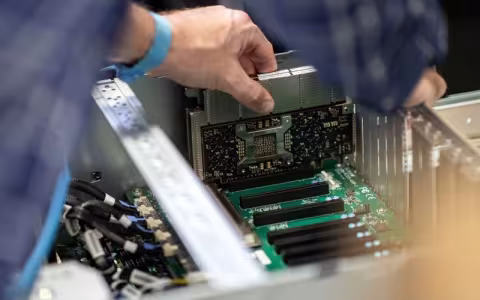 A close-up image of human hands inserting a silver and black computer card into a machine.