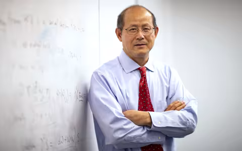 UAlbany Professor of Mathematics and Statsticis Kehe Zhu stands next to a white board.