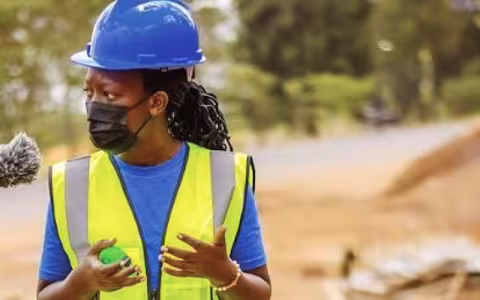 Berthe Rutagambwa discusses a construction project with microphone visible in foreground.