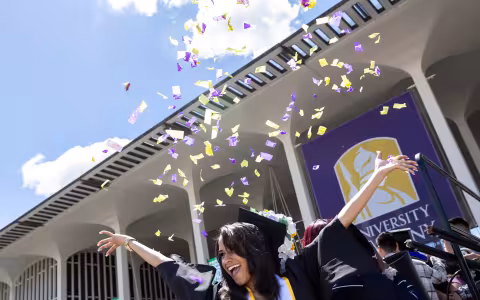 A student graduates from the university at albany as confetti flies around in the background.