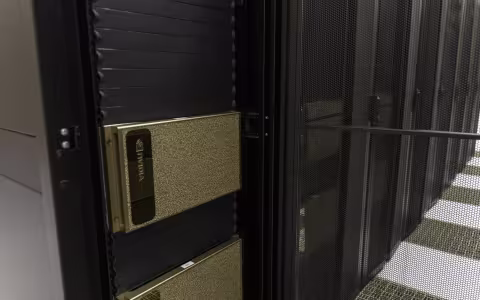 A close-up of a silver rectangular GPU system installed in a row of tall, black server racks. 
