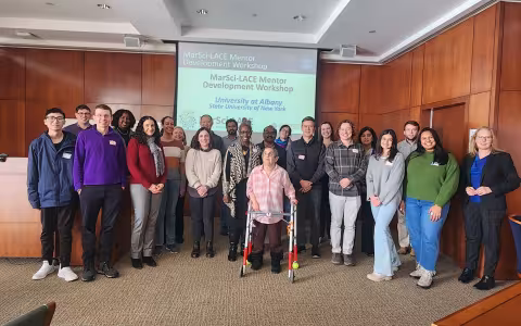 Faculty, staff and students stand in front of a presentation slide in the Standish Room at the Science Library.