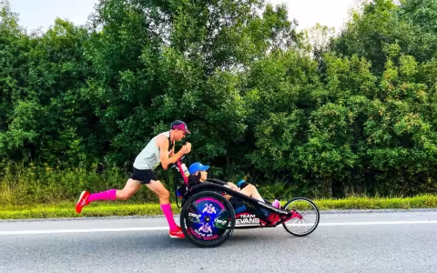 A runner pushes a peron seated in a racing chair along a road with greenery in the background
