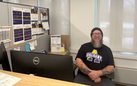 Man in UAlbany black T-shirt wearing beanie and glasses