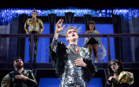 Student actors in hair, makeup and costume sing on stage.