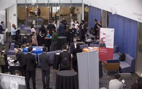 A group of people gathered around tables in a lobby, engaged in conversation and networking.