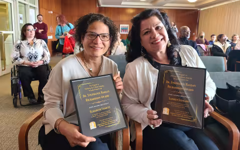 Dr. Elizabeth Vásquez and Dr. Carman Serrano sit while holding their awards.