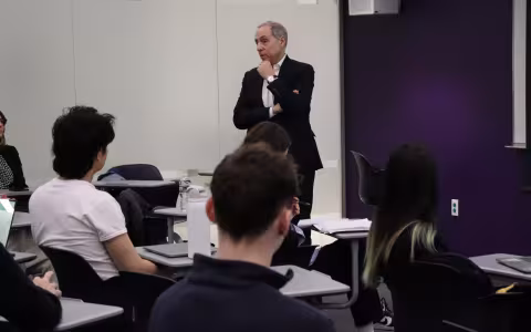 Man in a suit standing in front of a class of students. 