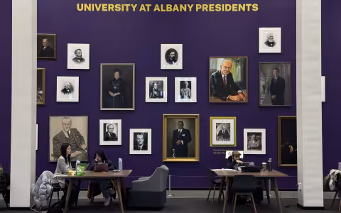 Students studying in front of the University at Albany Presidents Portrait Wall