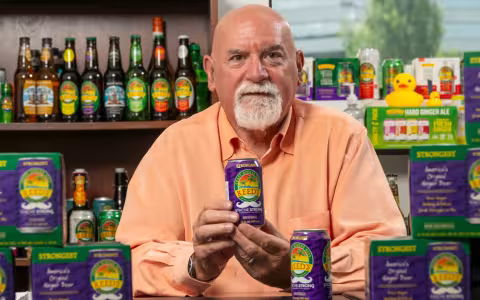 Norm Snyder sitting at a table filled with cans and bottles of Reed's soda. 