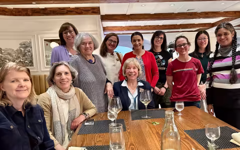 11 members of Women in Science and Health (WISH) pose for a photo around a restaurant table.