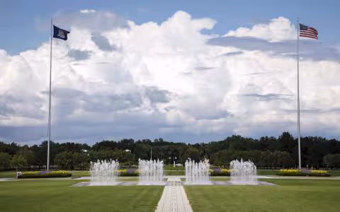 Flags wave in the wind and fountains spray water in the UAlbany entry plaza.