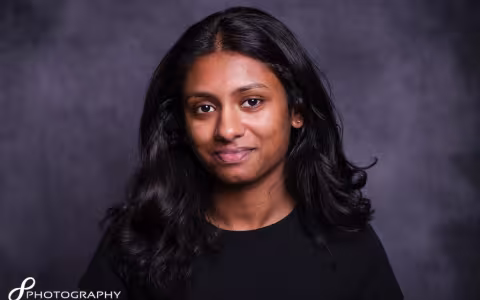 A young woman with long hair wearing a black shirt, looking confidently at the camera. 