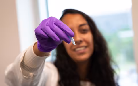 Sujata Murty holds up a crushed coral sample wearing a purple glove and lab coat.
