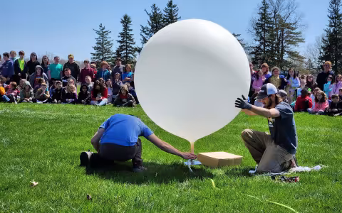 Mesonet intern Eric Creighton and technician Sam Cherubin prepare a weather balloon to launch in front of children at the Belleville Henderson Central School.