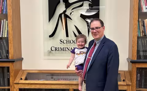 John McCluskey stands with his granddaughter in front of a sign for the School of Criminal Justice. 
