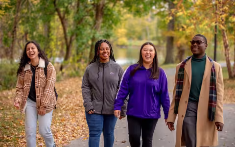 Four UAlbany students laughing while walking a fall colorful, foliaged path.