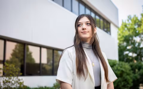Student Cassie Kane stands in front of the School of Public Health, looking to the side.
