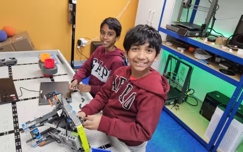 Two boys smile as they assemble a robot on a game board.