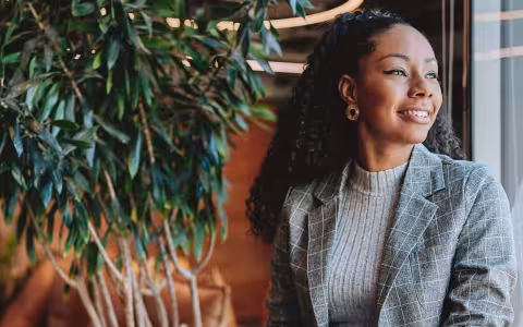 A smiling professional in communications or marketing sitting by a window holding a laptop.